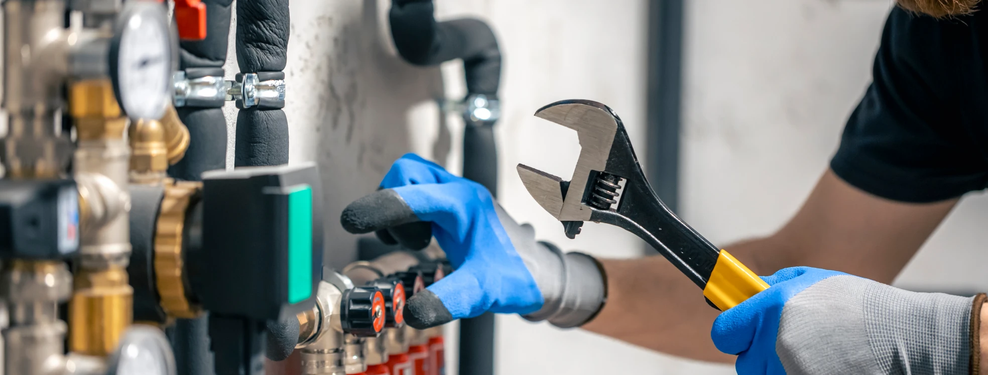 Technician wearing protective gloves using an adjustable wrench to service a complex plumbing valve system.
