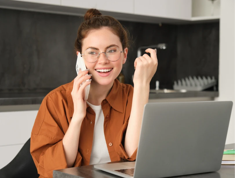Smiling woman on a phone call with a laptop, possibly discussing home services like plumbing, in a modern home setting.