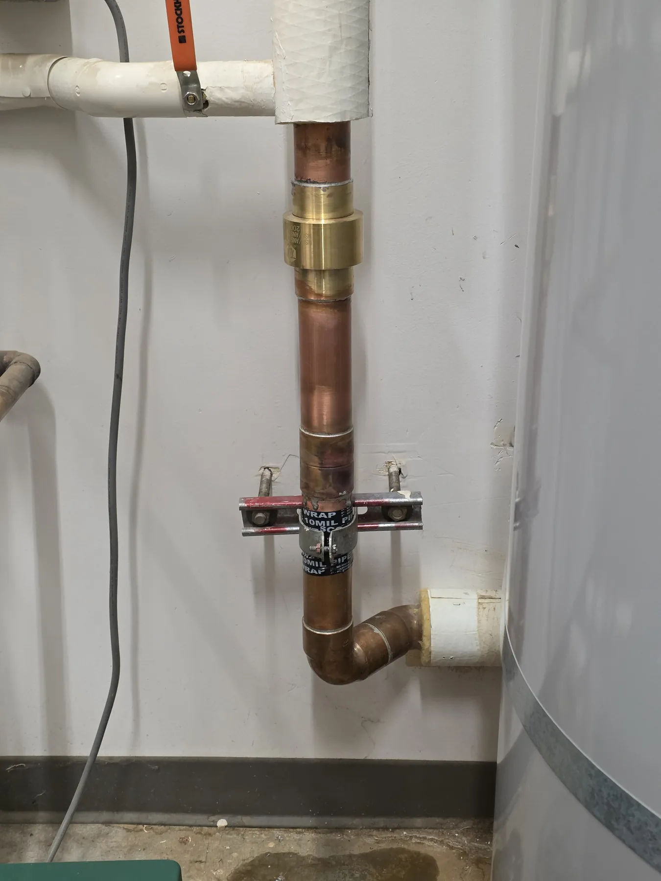 A copper water line with a new brass fitting, clamped to a white wall