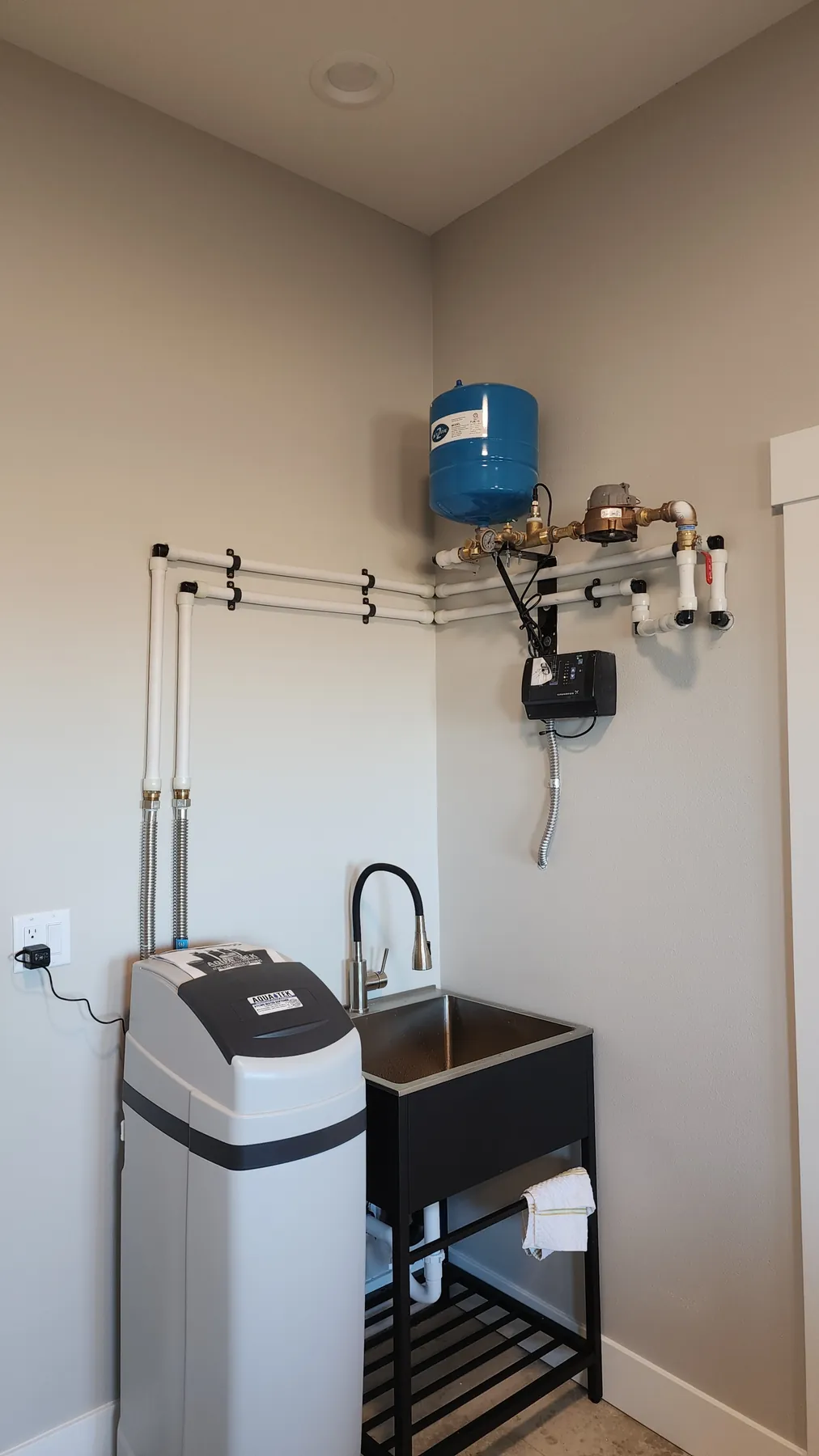 A water softener beside a utility sink, with the water lines and a blue tank on the wall above