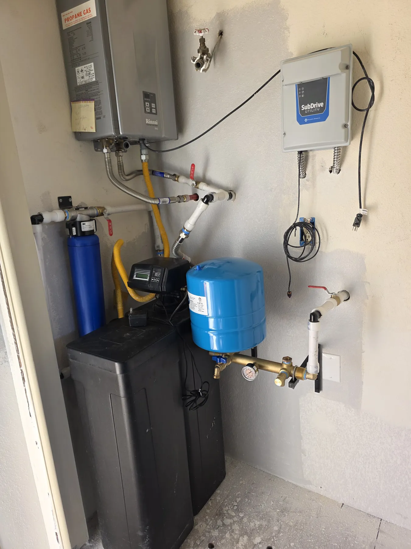A water softener, blue filter housing and expansion tank plumbed beside a tankless water heater