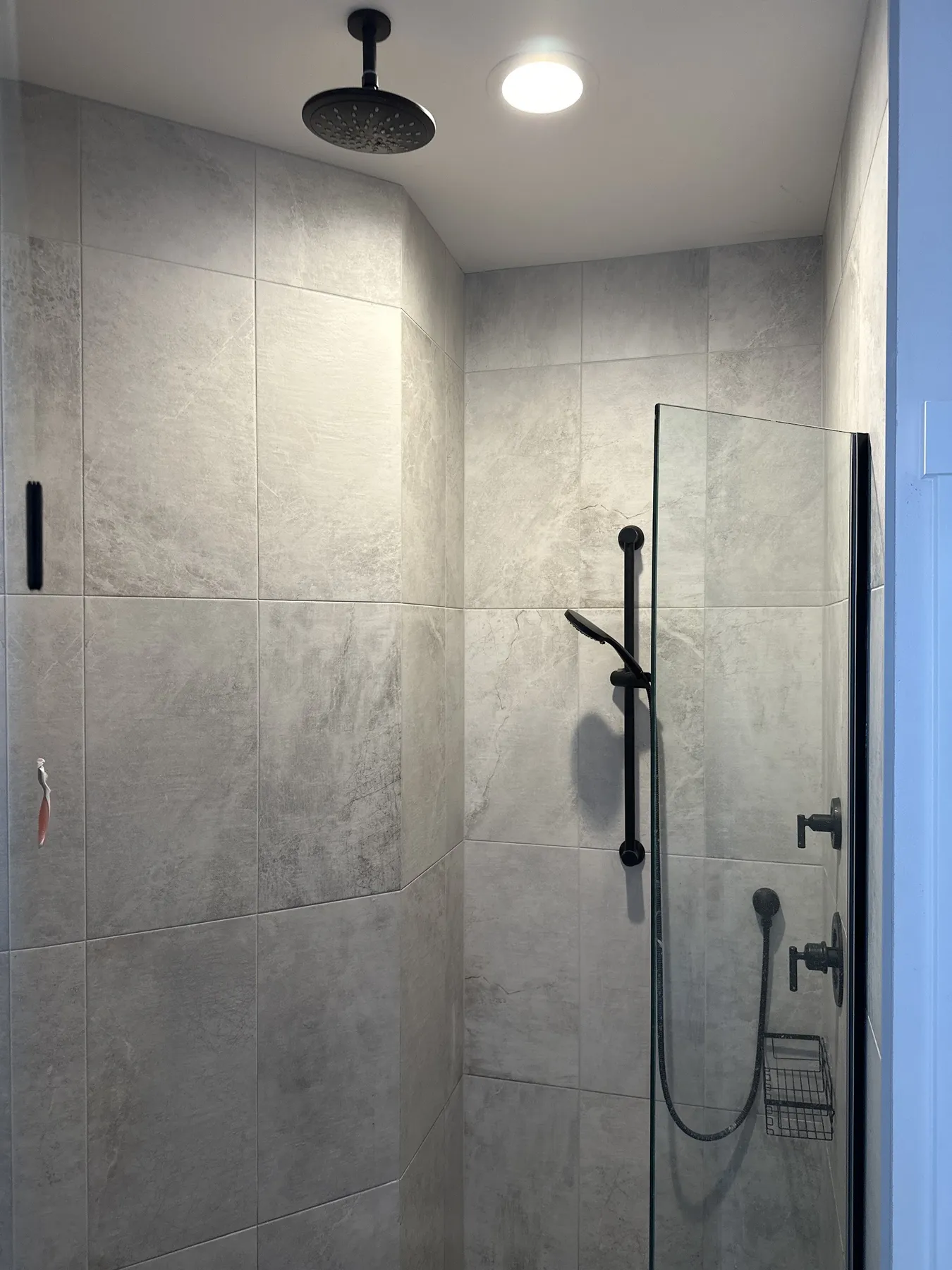 A finished walk-in shower with large gray tile, a rain head and a glass panel