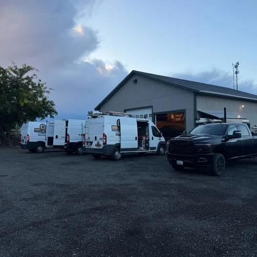 White work vans and a pickup parked outside a shop building at dusk